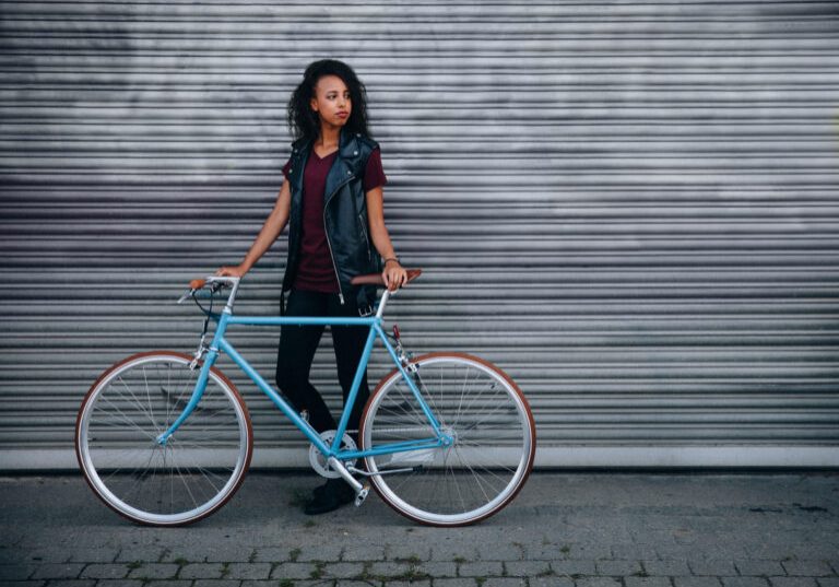 African American teenage girl standing on a city street with her fixed gear bicycle in front of urban graffitti